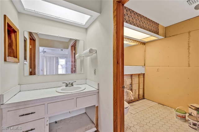 half bath with visible vents, toilet, a ceiling fan, a skylight, and vanity