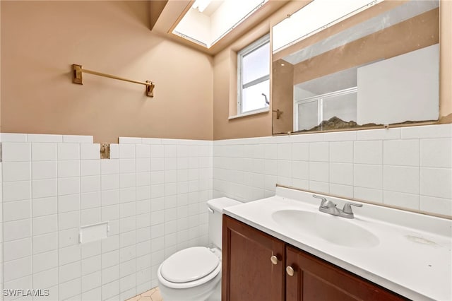 bathroom with a wainscoted wall, toilet, vanity, a stall shower, and tile walls