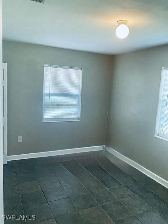 empty room with baseboards and dark tile patterned flooring