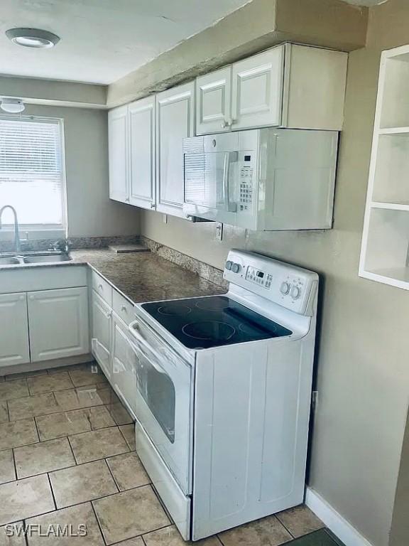 kitchen with baseboards, light tile patterned floors, white cabinets, white appliances, and a sink