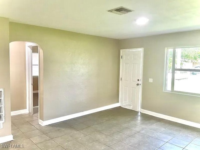 empty room featuring visible vents, arched walkways, baseboards, and light tile patterned flooring