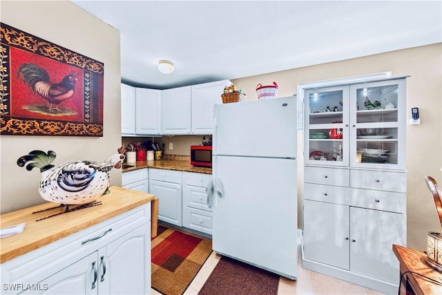 kitchen with white cabinets, wooden counters, and freestanding refrigerator