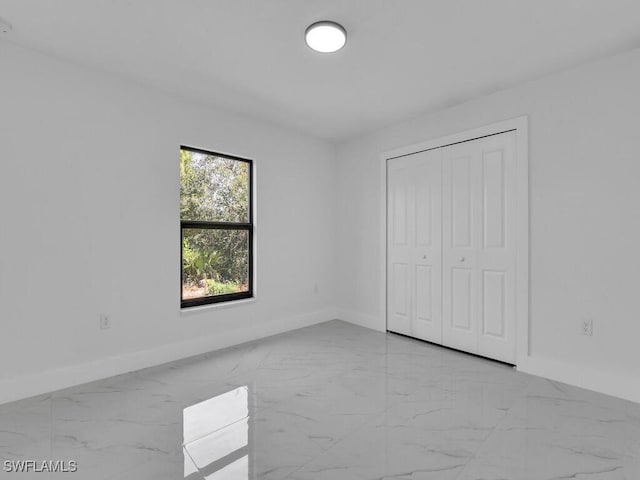 unfurnished bedroom with marble finish floor and baseboards