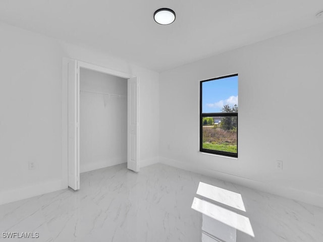 unfurnished bedroom featuring a closet, marble finish floor, and baseboards