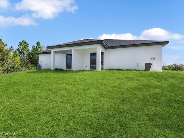 rear view of house with a lawn and stucco siding