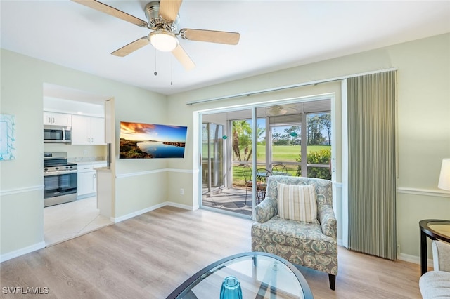 living area featuring baseboards, light wood-type flooring, and a ceiling fan