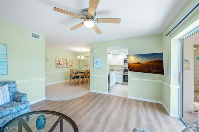 living room featuring visible vents, ceiling fan with notable chandelier, baseboards, and light wood-style floors