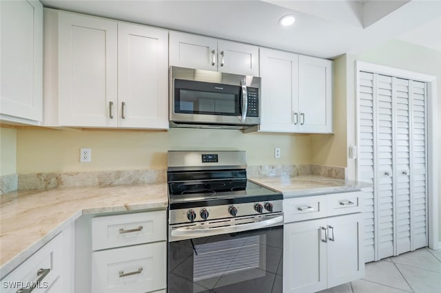 kitchen with light tile patterned floors, stainless steel appliances, light stone countertops, and white cabinetry