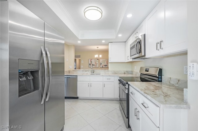 kitchen with appliances with stainless steel finishes, an inviting chandelier, crown molding, light tile patterned floors, and a raised ceiling