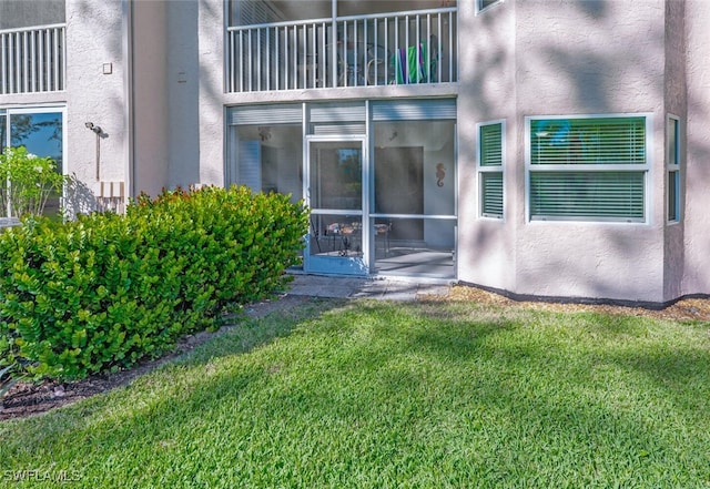 property entrance featuring a balcony, a yard, and stucco siding