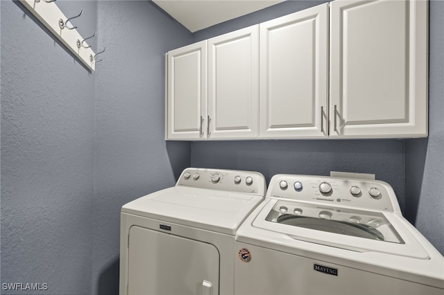 washroom featuring washer and dryer, cabinet space, and a textured wall