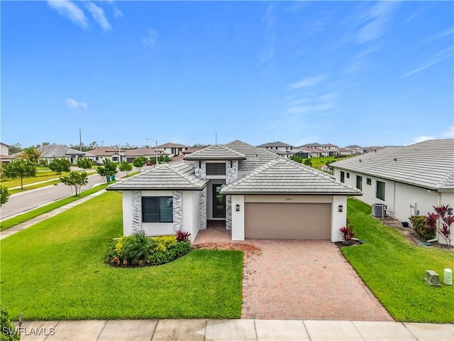 view of front of property featuring a garage, cooling unit, decorative driveway, and a front lawn