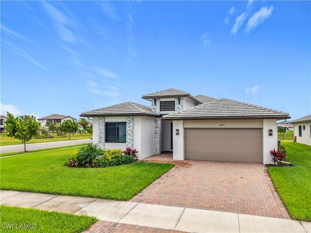 prairie-style home with a front lawn, decorative driveway, an attached garage, and stucco siding