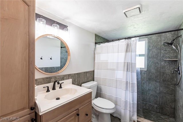 bathroom with visible vents, a wainscoted wall, toilet, tiled shower, and vanity