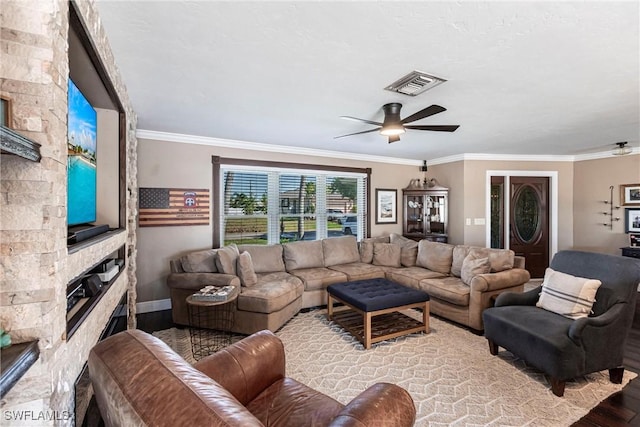 living area featuring visible vents, a ceiling fan, wood finished floors, a stone fireplace, and crown molding