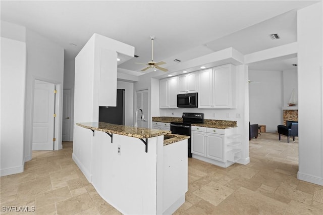 kitchen featuring visible vents, a breakfast bar, dark stone counters, ceiling fan, and black appliances