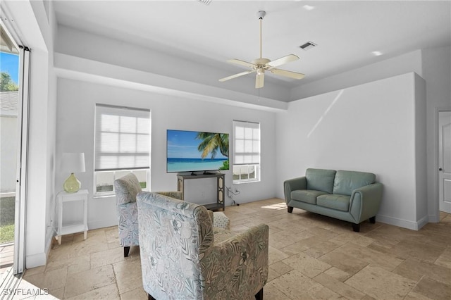 living room featuring stone tile flooring, visible vents, baseboards, and a ceiling fan