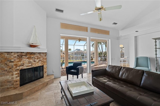 living area with a glass covered fireplace, a ceiling fan, visible vents, and stone tile flooring