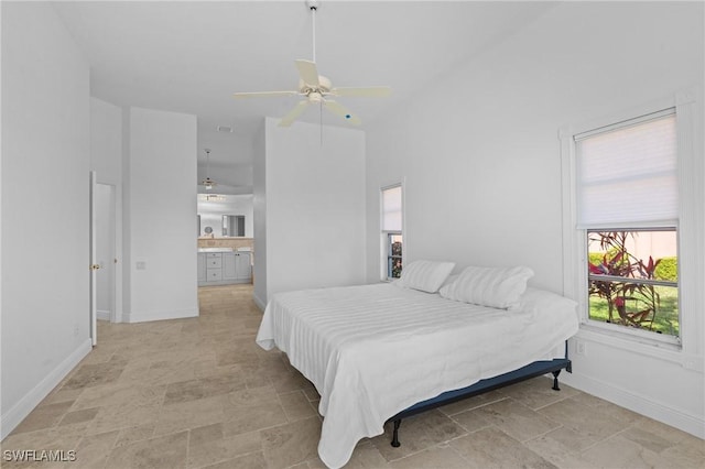 bedroom featuring ensuite bath, stone finish floor, a ceiling fan, and baseboards