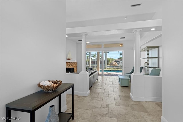 corridor featuring baseboards, visible vents, ornate columns, and stone tile flooring