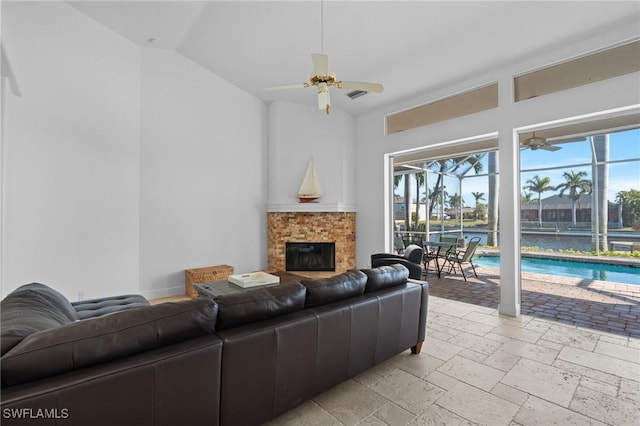 living room with baseboards, ceiling fan, lofted ceiling, a fireplace, and stone tile flooring