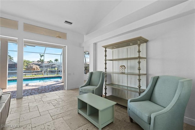 living area with visible vents, baseboards, stone tile floors, and vaulted ceiling