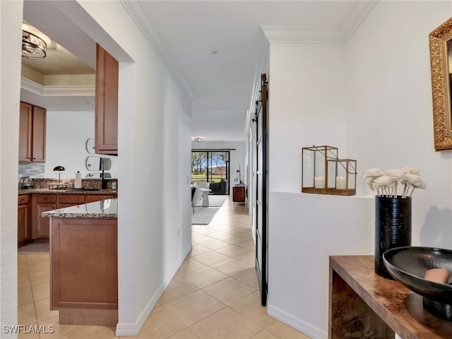 corridor with light tile patterned flooring, baseboards, crown molding, and a barn door