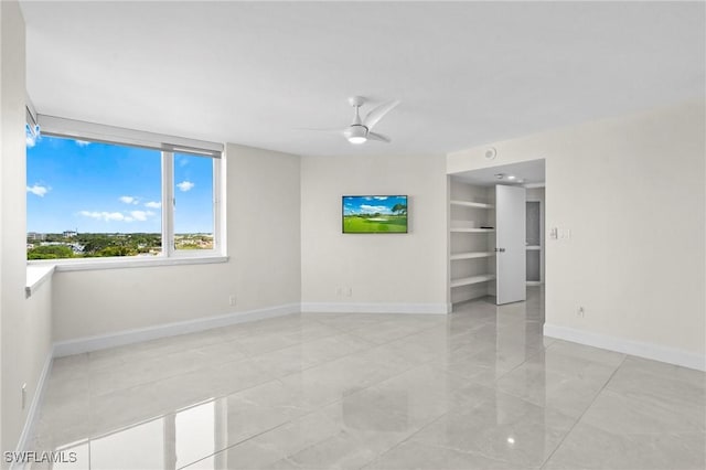 spare room with built in features, baseboards, and a ceiling fan