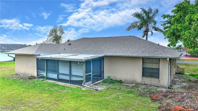 back of property with stucco siding, a lawn, a sunroom, and roof with shingles