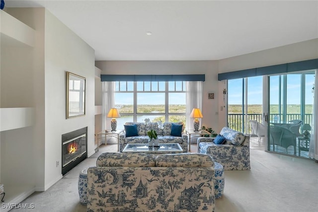living room with baseboards, a water view, a glass covered fireplace, and light colored carpet