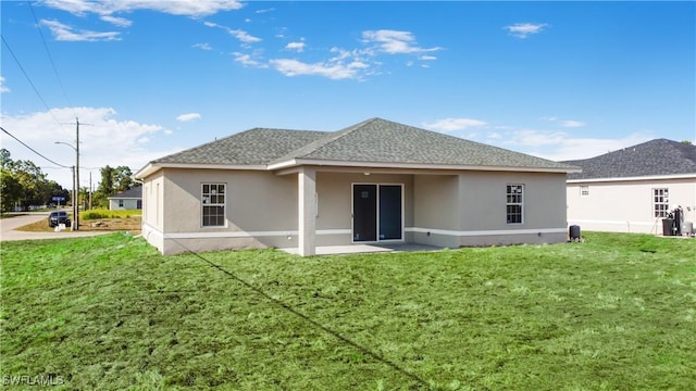 back of house with a yard, a shingled roof, and stucco siding