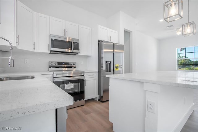 kitchen featuring a sink, stainless steel appliances, light wood finished floors, white cabinetry, and light stone countertops