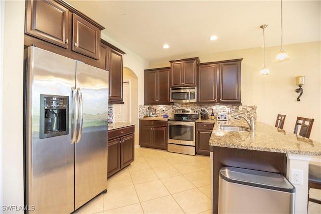 kitchen featuring a sink, tasteful backsplash, stainless steel appliances, dark brown cabinetry, and a peninsula