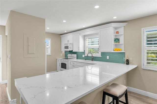 kitchen with light wood-style flooring, a sink, tasteful backsplash, white appliances, and light stone countertops