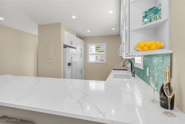 kitchen with a sink, light stone counters, white appliances, white cabinetry, and open shelves