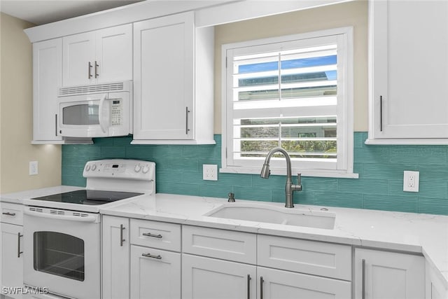 kitchen with a sink, light stone counters, white appliances, white cabinets, and decorative backsplash