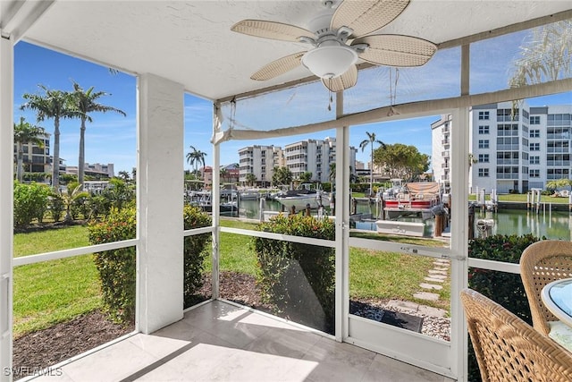 sunroom with a view of city, a ceiling fan, and a water view