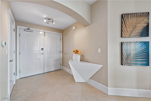 foyer entrance featuring light tile patterned floors, baseboards, and arched walkways