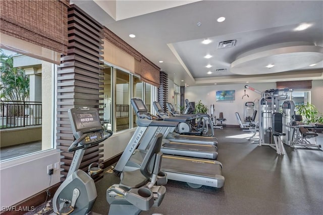 exercise room featuring a raised ceiling, recessed lighting, visible vents, and baseboards