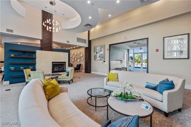 living area featuring visible vents, carpet floors, a high ceiling, a fireplace with raised hearth, and a notable chandelier