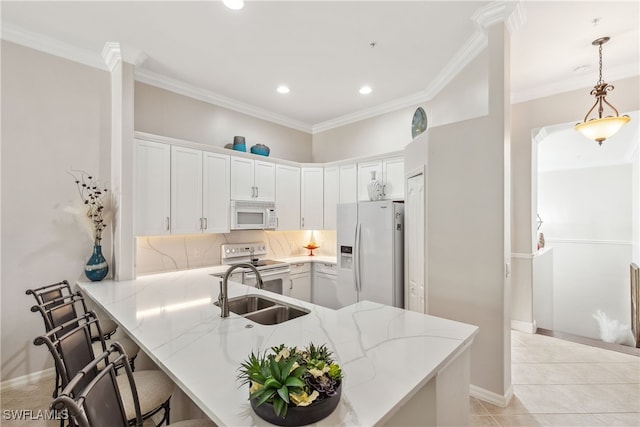 kitchen with white appliances, a peninsula, ornamental molding, a sink, and a kitchen breakfast bar