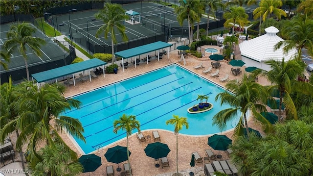 pool featuring glass enclosure, a patio, a community hot tub, and fence