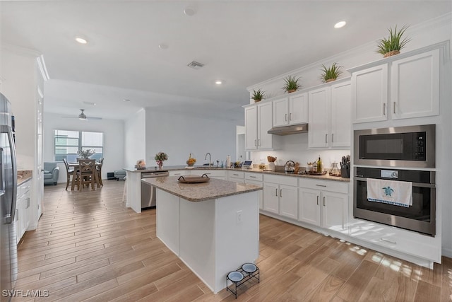 kitchen with light wood finished floors, a peninsula, ceiling fan, appliances with stainless steel finishes, and white cabinetry