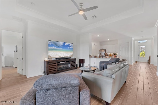 living area featuring a raised ceiling, crown molding, visible vents, and light wood-type flooring