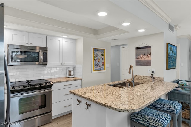 kitchen with backsplash, light stone counters, appliances with stainless steel finishes, a peninsula, and a sink