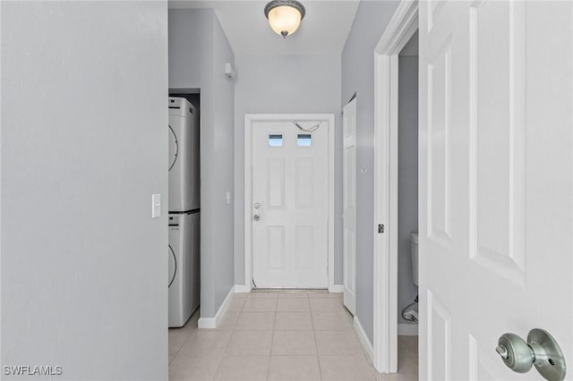 hallway featuring light tile patterned floors, stacked washer / dryer, and baseboards