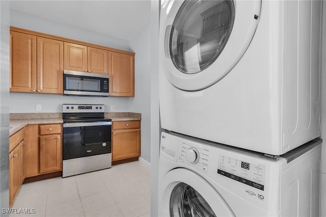 kitchen with light tile patterned floors, brown cabinetry, light countertops, appliances with stainless steel finishes, and stacked washer / dryer