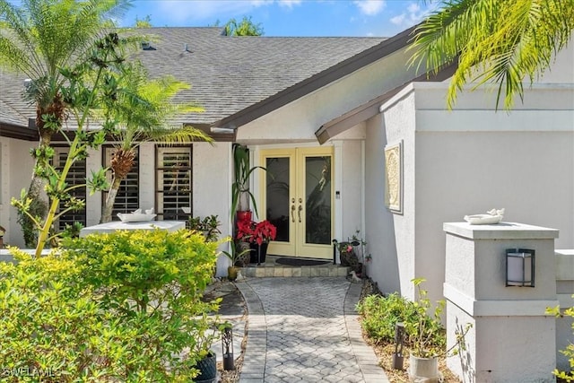 entrance to property featuring french doors, roof with shingles, and stucco siding