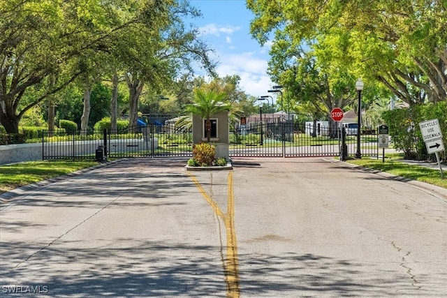 view of road with a gate, traffic signs, curbs, street lighting, and a gated entry