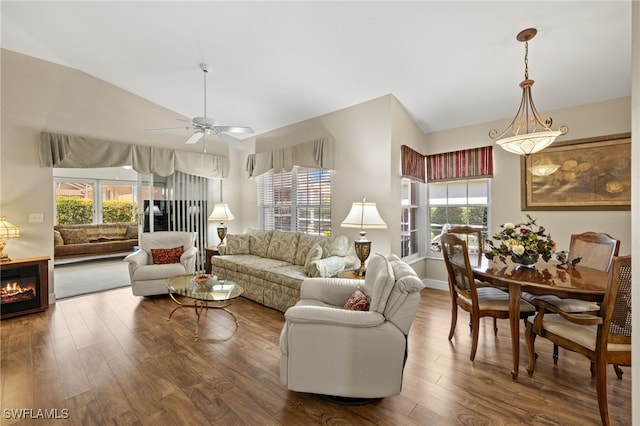 living area with a warm lit fireplace, wood finished floors, a ceiling fan, and vaulted ceiling